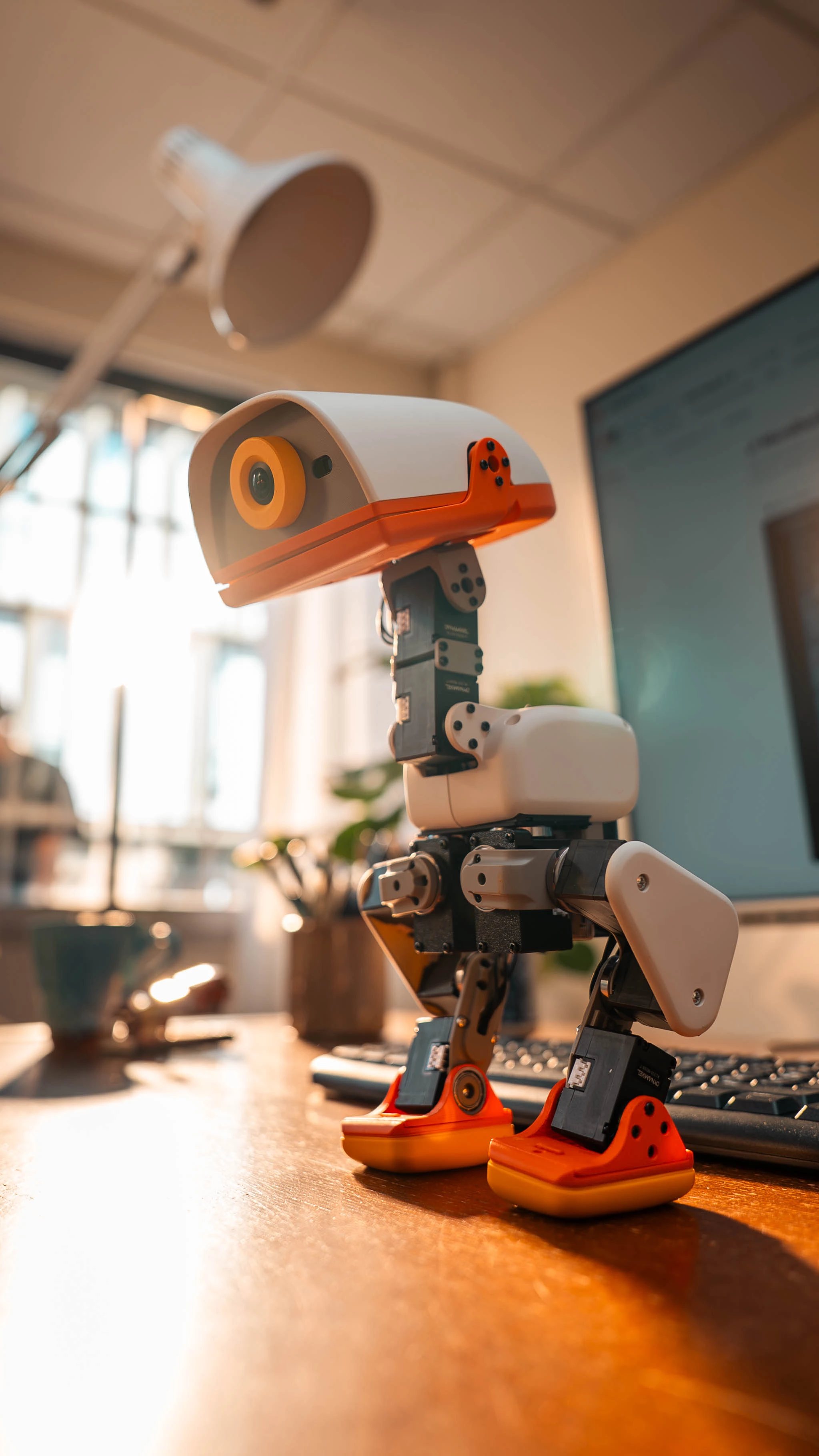 Microduck robot standing on a desk with its camera and articulated joints visible