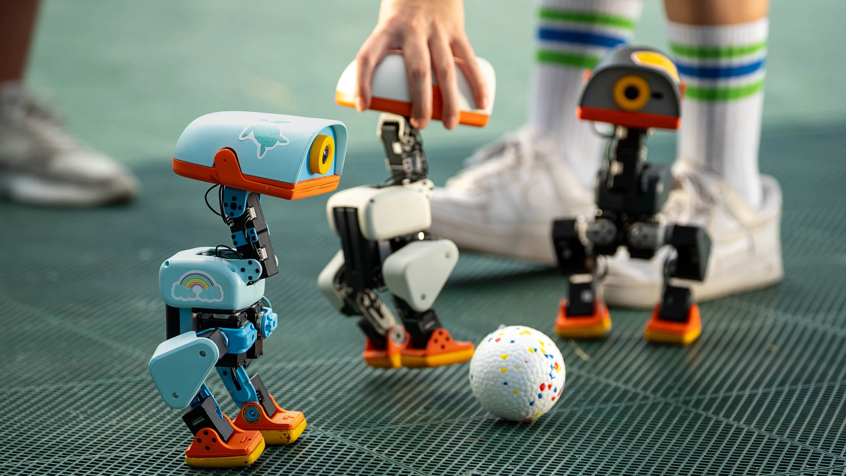 Three Microduck robots gathered around a ball on a playing surface