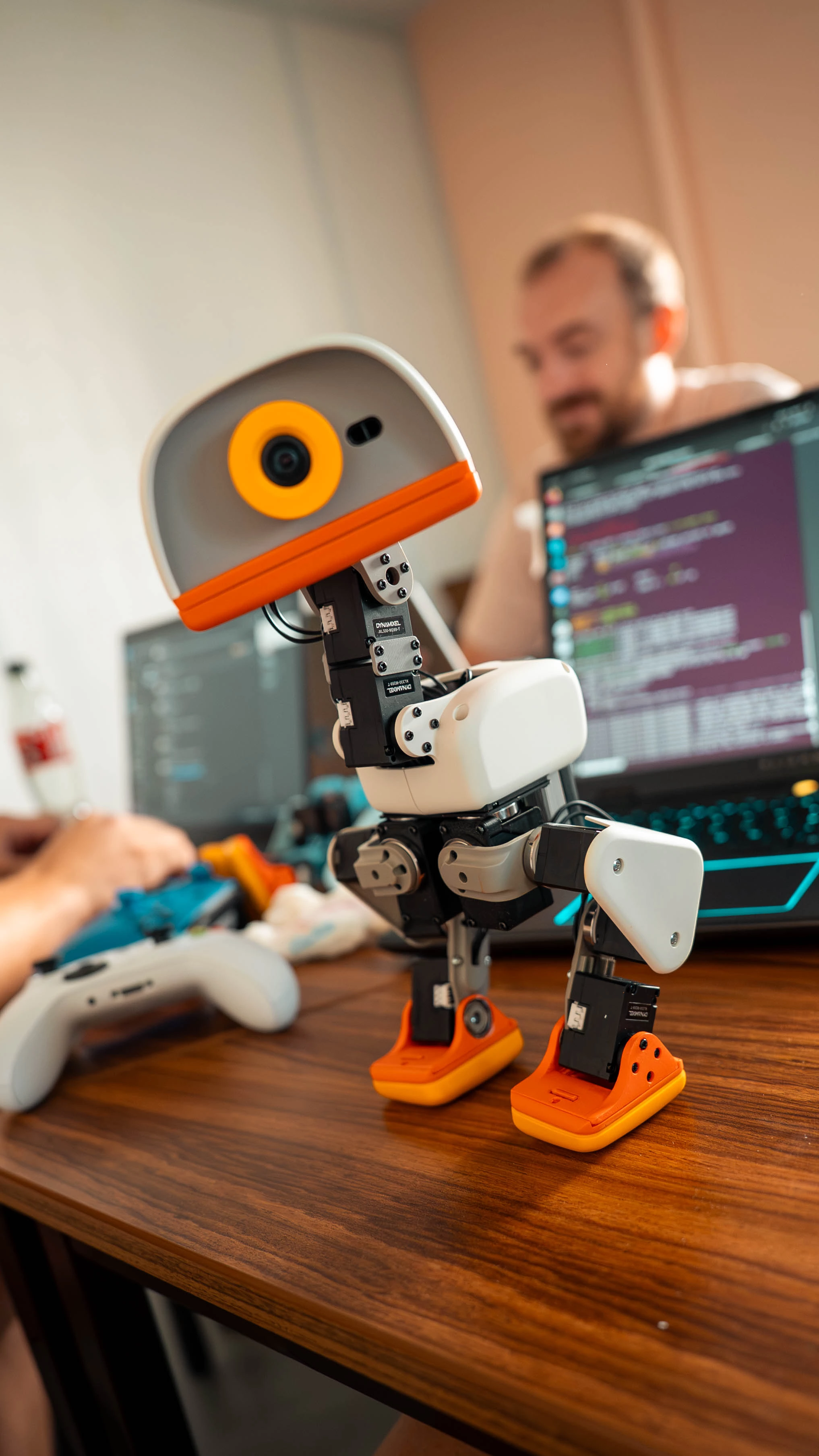 Microduck robot on a desk with a developer working on a computer behind it