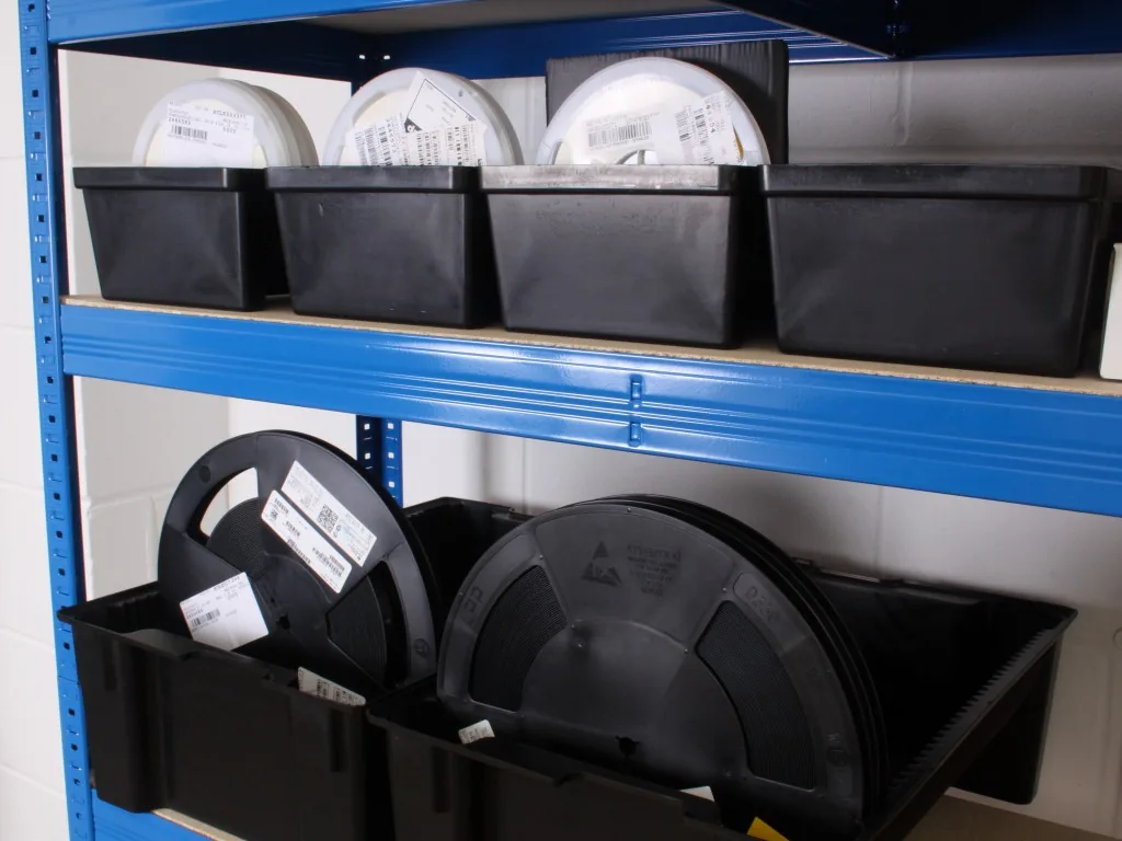 Component reels stored in labeled bins on a stockroom shelf