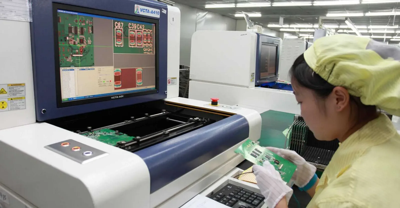 AOI operator reviewing solder joint inspection results on screen beside an automated optical inspection machine